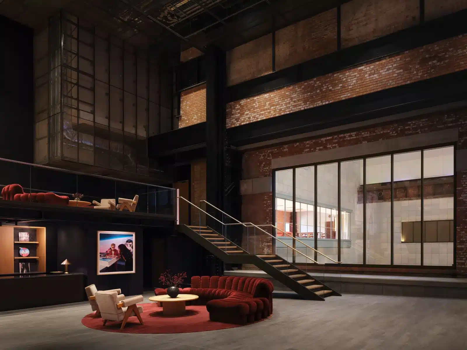 Double-height foyer with exposed steel and brick, a staircase, a large glass window and a round red sofa