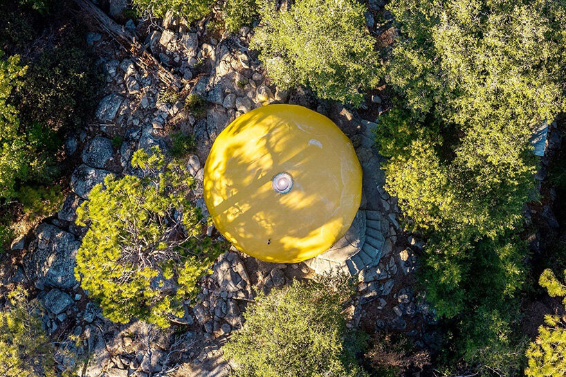 Aerial view of the round yellow roof of the Donaldson Futuro among trees and rocks