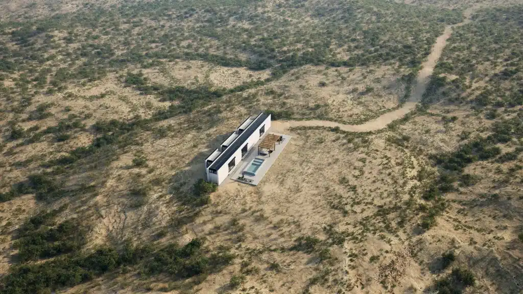 Aerial view of the elongated white Monocabin XL5 house in desert scrubland with a dirt road