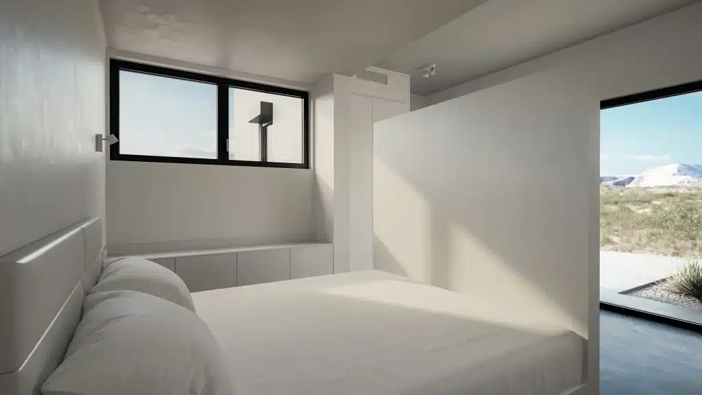 Minimal white bedroom in Monocabin XL5 with a horizontal window and a glass door onto the desert