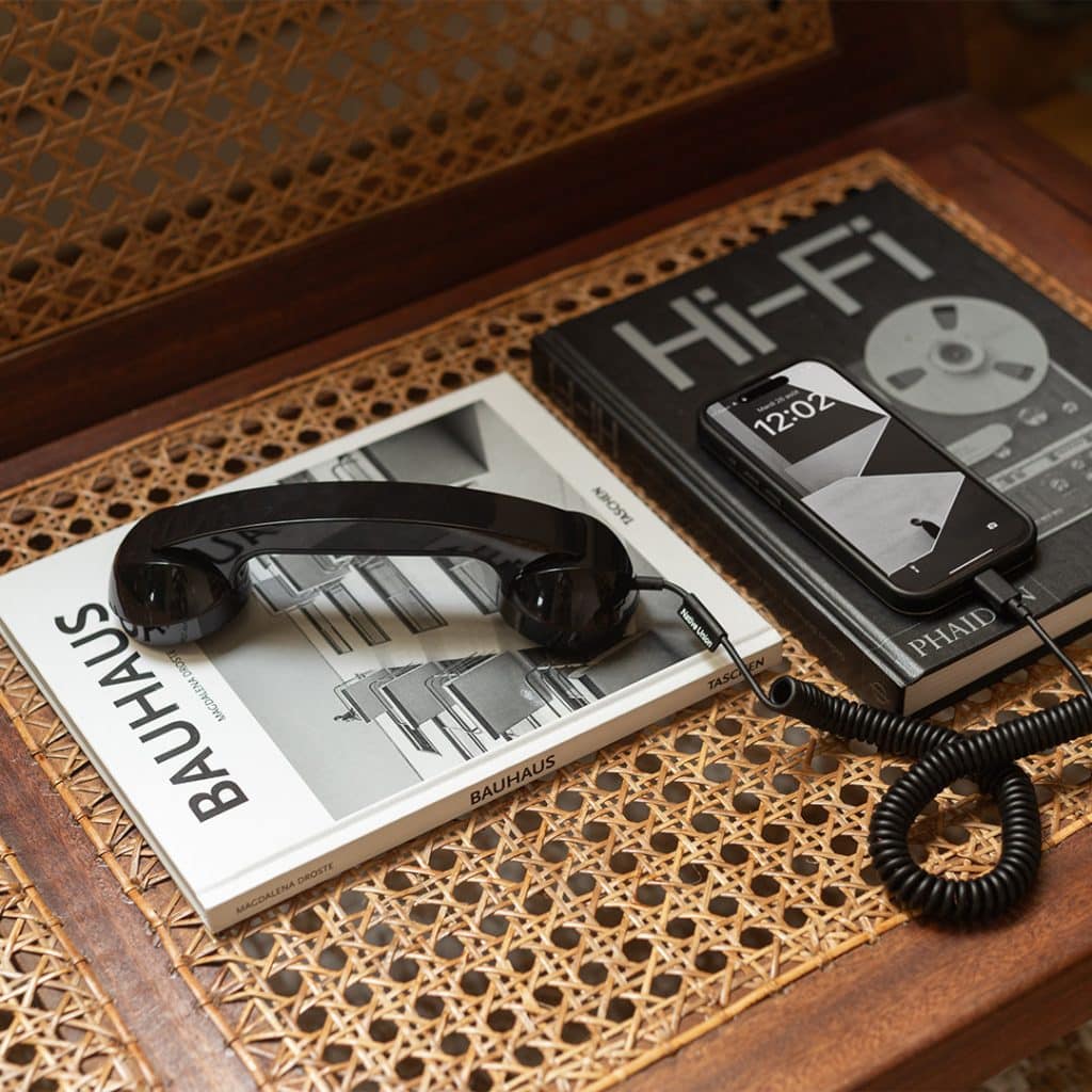 Black Native Union POP Phone handset on a cane chair next to design books and a smartphone