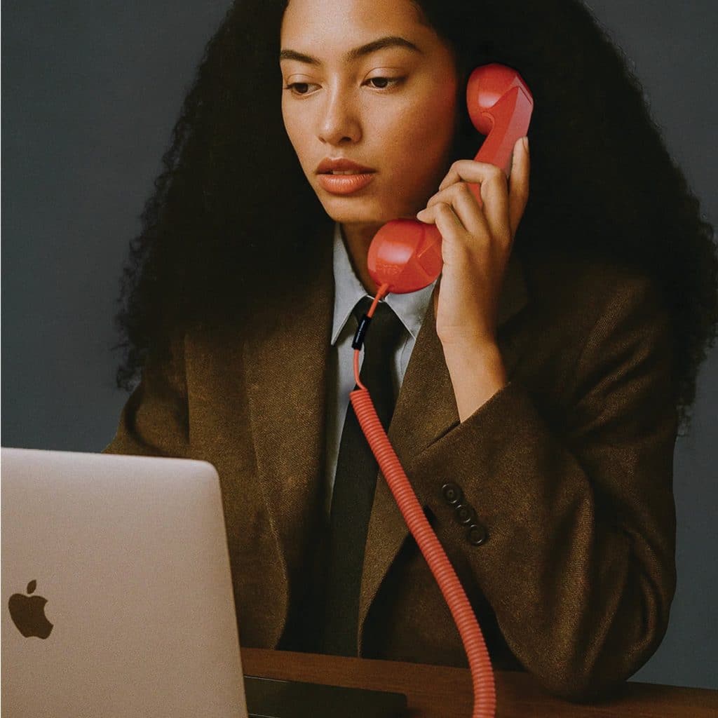 Woman in a blazer talking on a red Native Union POP Phone handset in front of a laptop