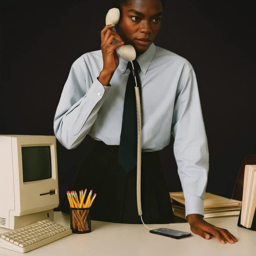 Man in shirt and tie on a cream Native Union POP Phone handset at a desk with a vintage computer