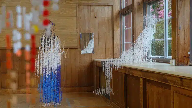 Seen from the right angle, hundreds of hanging beads form a child leaning on the windowsill